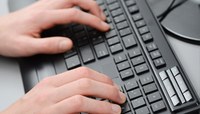Mãos trabalham sobre teclado de computador.