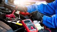Técnico com luvas utiliza multímetro ao trabalhar na manutenção de um carro.