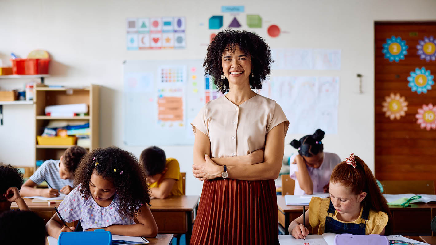 Professora sorri em sala de aula de educação infantil com seus estudantes