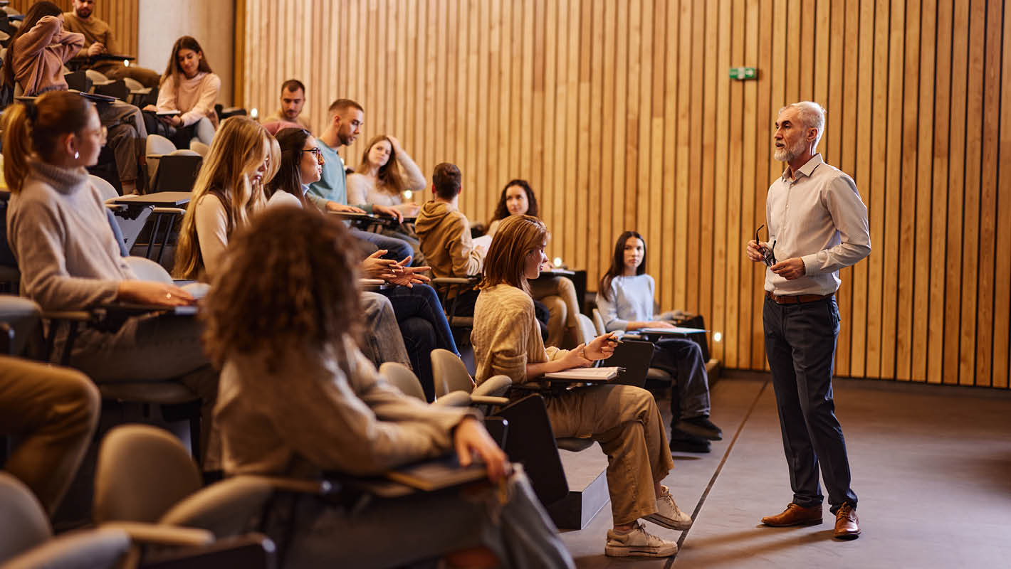 Professor ministra aula diante de turma em auditório.