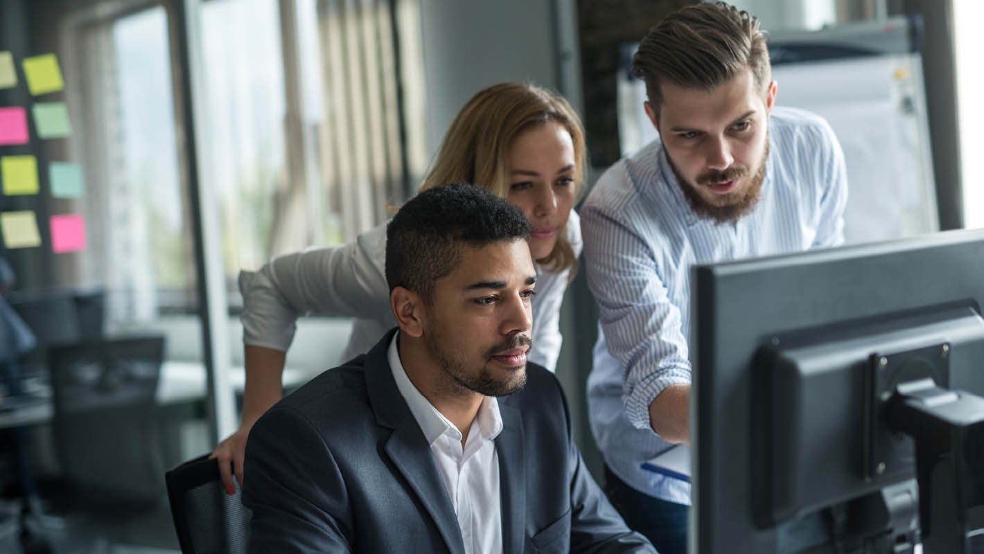 Dois homens e uma mulher com roupas sociais trabalham juntos em projeto no computador