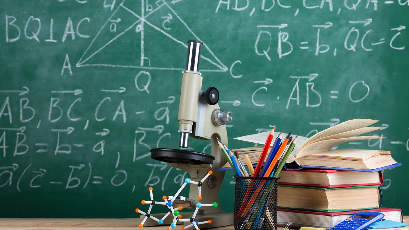 Quadro negro com fórmulas ao fundo, microscópio, livros, modelo de moléculas e lápis coloridos